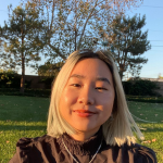 Melinda, a young East Asian person with chin-length bleached gray hair, is wearing a black turtleneck shirt and smiling