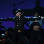 Female Amateur Night Contestant wearing black jacket, black pants, and a black cap with arms outstretched on Apollo Stage
