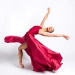 Single dancer in red dress in standing fourth position cambre back.