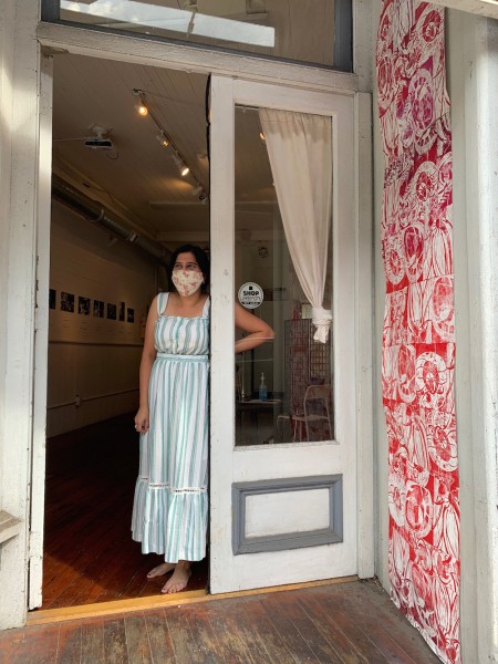 A woman stands in a blue dress in an open doorway, leading into a storefront art gallery.