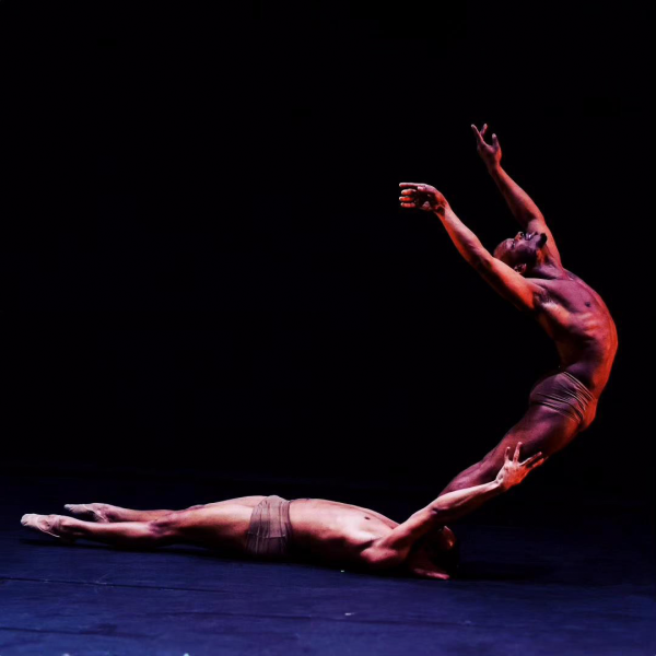 Photograph of two dancers: one laying on the ground and steadying another who leans back gracefully with arts outstretched 