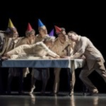 Seven Performers seating on a table - The Road Awaits Us, choreography by Annie-B Parson 