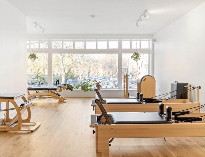 a white studio with wooden floors and with various pilates and gyrotonic equipment. windows in the back 