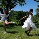 Two dancers dressed in white are captured mid-spin, their feet skimming the grassy field