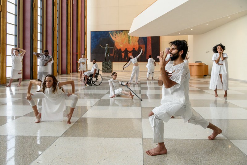 Physically diverse living human sculptures dressed in white. 
