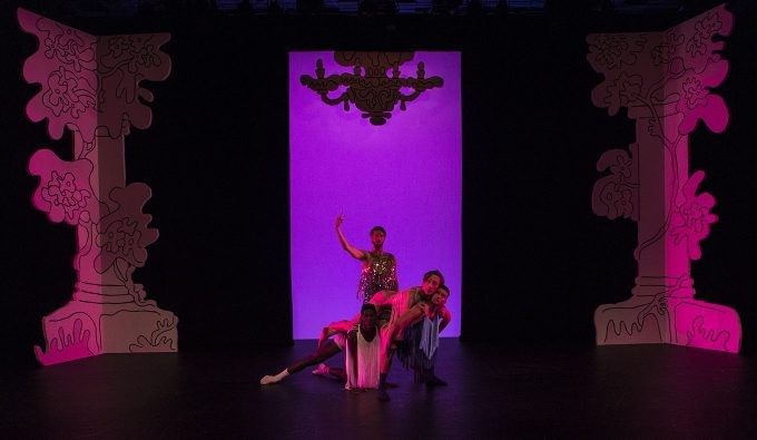In between two columns, are four dancers on different levels in front of a purple back drop