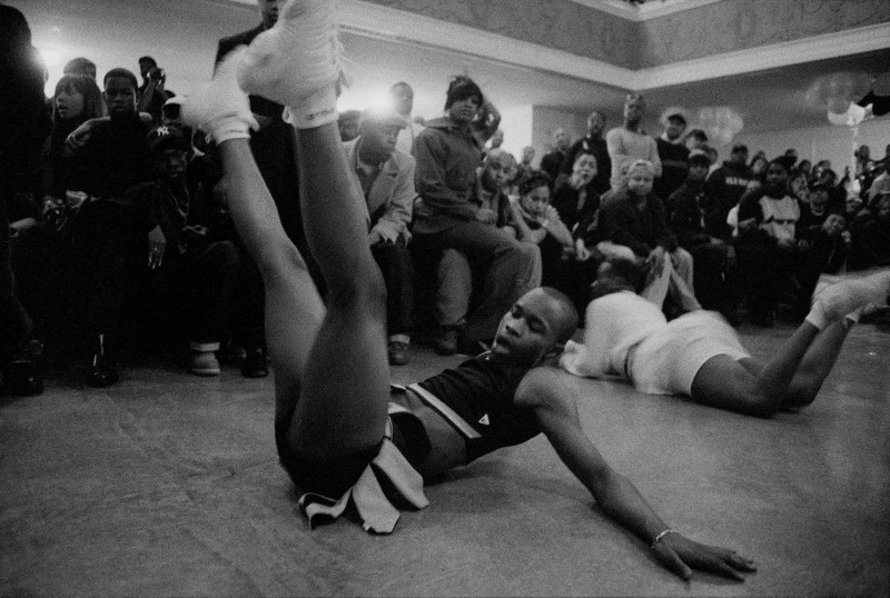 In a black-and-white picture, a performer in possibly a cheer leading outfit lays on the floor caught in the middle of dancing.