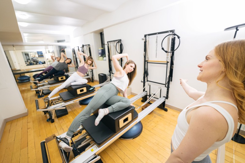 Pilates reformer class with 4 participants being taught by a trainer