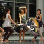 3 dancers wave a piece of quilted textile art as 1 dancer moves through it