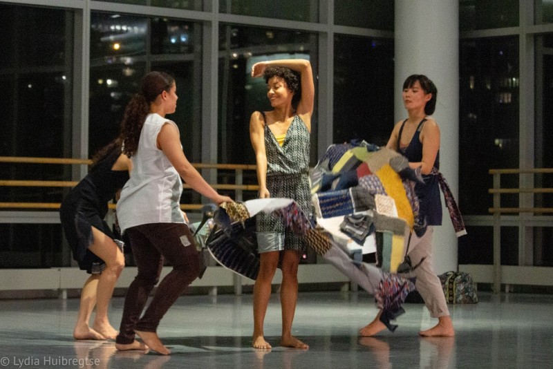 3 dancers wave a piece of quilted textile art as 1 dancer moves through it