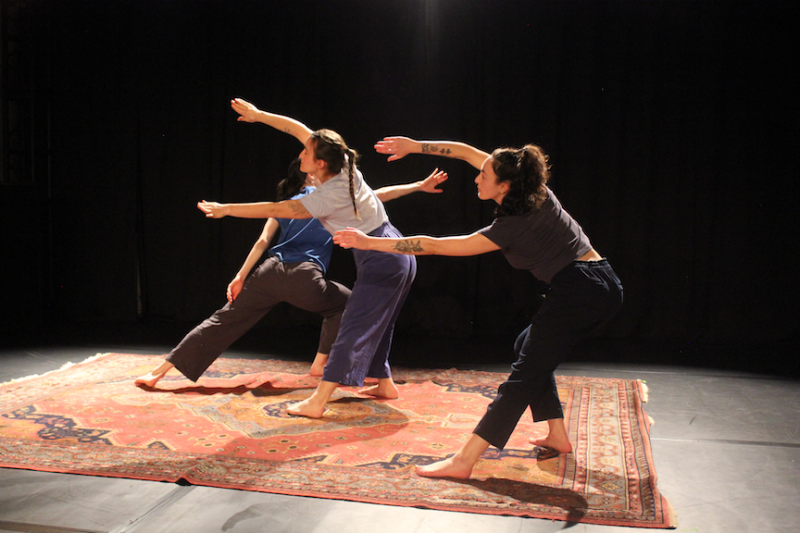Three dancers, two in the foreground with arms outstretched & one partially visible behind, are dancing on a rug at the BAC