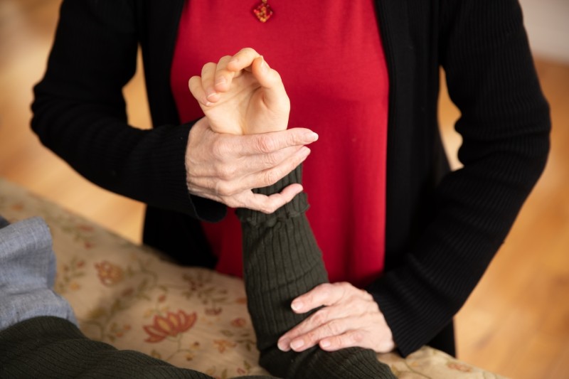 Two hands support a student's lower arm as it extends toward the ceiling.