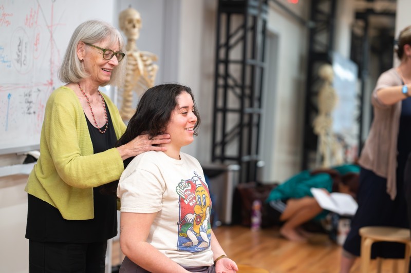 Ann Rodiger, standing, places her hands along the neck of a seated student during a workshop at the Balance Arts Center