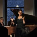 A woman stands in front of a piano while singing during a workshop at the BAC