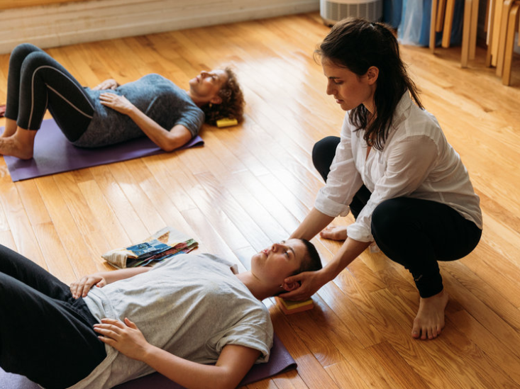 A student laying semi-supine on the floor while and Alexander Technique teacher has her hands on her head.