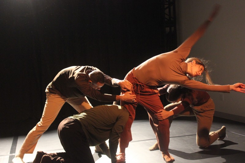 3 dancers grab the legs of a 4th dancer who is standing and reaching her body sideways during a performance at the BAC