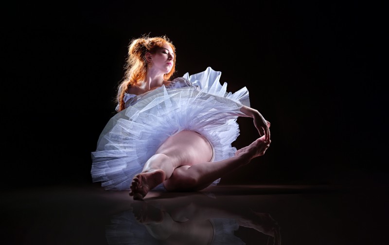 Ballerina sitting illuminated from behind with a glow around the shilouette 