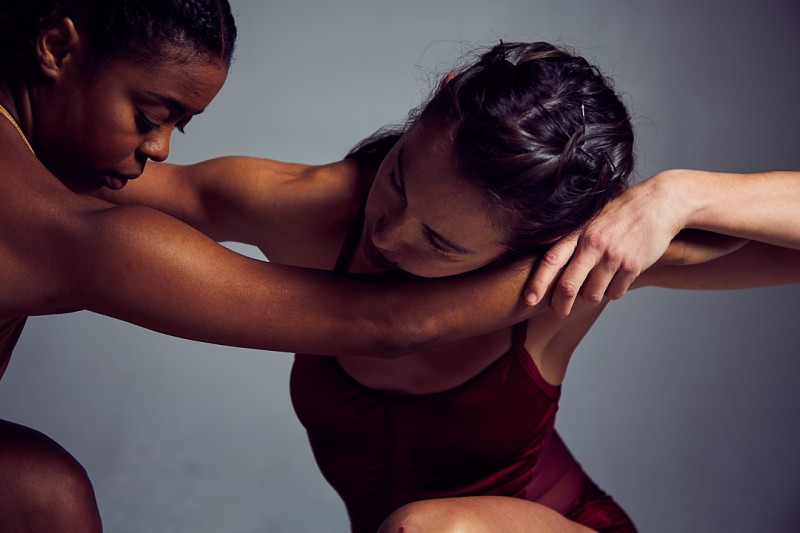 african american women extending hands to women of european decent, holding hands at a distanced embrace