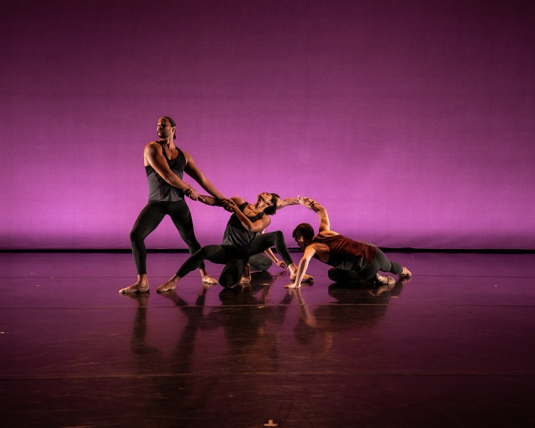 Photo of four male dancers on stage with purple backdrop lighting