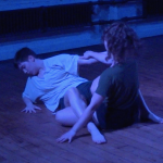 Two dancers embracing while sitting on the floor. From "Hineni" performed in Fertile Ground.