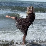 A dancer wearing a flowing, brown dress splashes in the ocean.