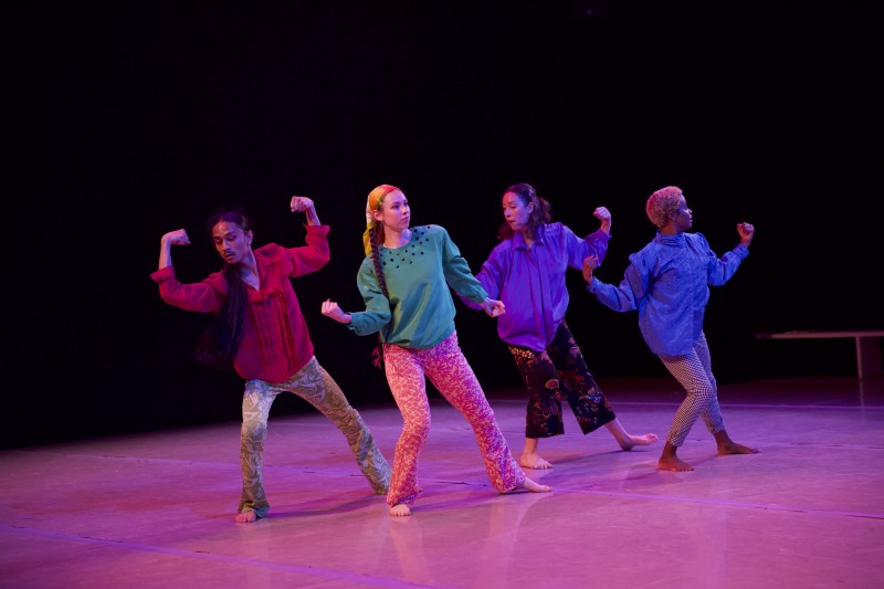4 dancers on stage in colorful clothing, elbows bent in a variety of muscle poses, expressions of care in their eyes.