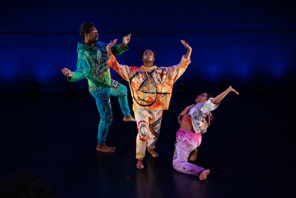 Three black performers in vibrant sweatsuits frame each other and refer to the stars
