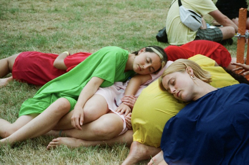 multiple bodies lying on grass intertwined, wearing block colored outfits 