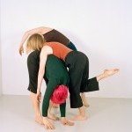 Three dancers fold on top of each other. One dancer has bright pink hair