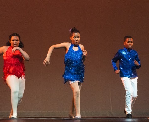 3 young Dominican Latin dance students on stage wearing red and blue - two girls and one boy