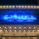 A photograph of an ornately tiled 1914 theater marquee with a blur neon sign that reads "Gene Kelly Billy Strayhorn"