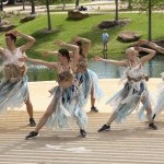 A photo of five dancers wearing costumes made of recycled plastic bags. They all lunge in one direction with their arms up.