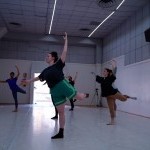 Dancers in a studio with their leg raised to the back and arms rounded.