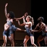 A Black dancer reaches high, while three other dancers support her limbs.