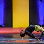 A dancer dressed in yellow leggings and a black shirt hinges backward