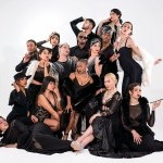 A group of performers in all black strike a pose