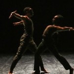 Two dancers, one with an ancient mask, perform a duet, lunging towards each other with their arms thrown back