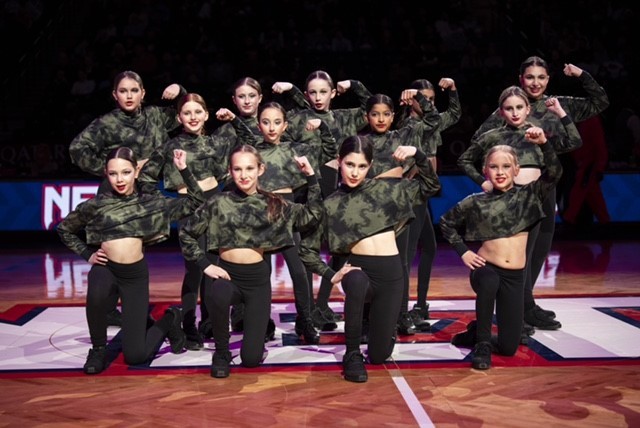 Energetic young dancers posing on the Court at Barclays Center in Brooklyn wearing black pants and camo tops.