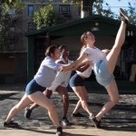 Three dancers dancing outside with one dancer lifting one leg