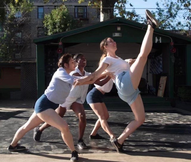 Three dancers dancing outside with one dancer lifting one leg