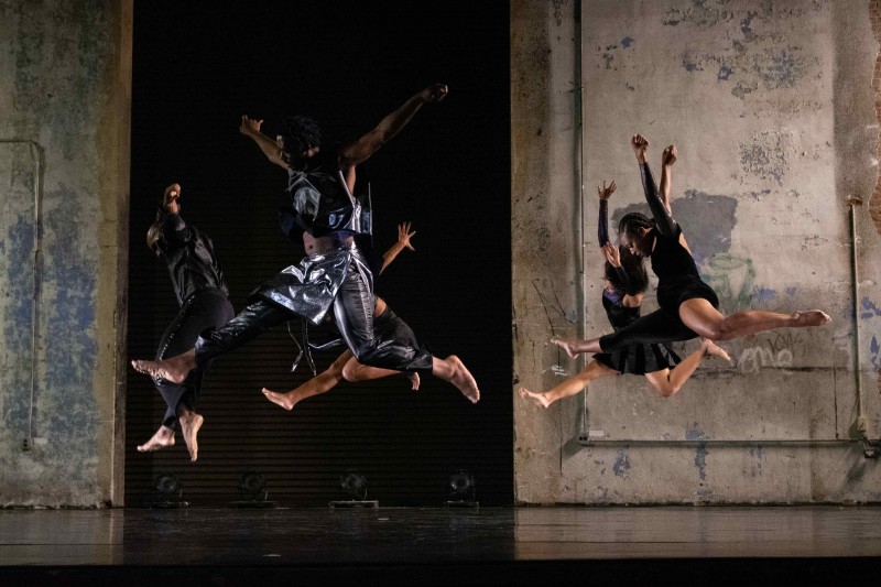 Dancers on stage jumping, with exposed brick wall