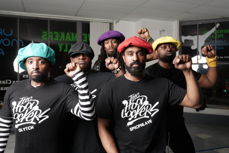 5 people in matching shirts and various hats holding up a fist