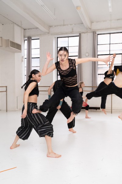 Dancer in black outfit jumping off other dancer, facing forward