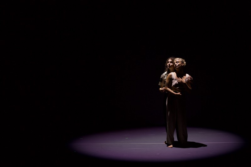 Two people stand in a pool of light embracing