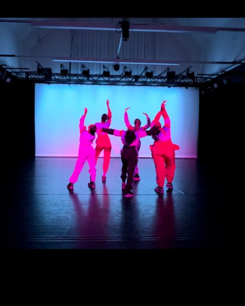 image of five dancers reaching wearing bright multicolored jumpsuits