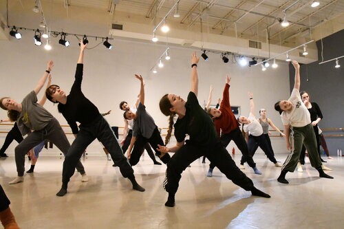 Dancers in a white studio face the front and bent to the left in a lunge reaching up with the right arm