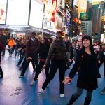 a diagonal line of dancers extend their hands to the ground. Wintertime in Times Square