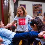 Teaching Artist with arms outstretched towards two young dancers in a backbend lift.