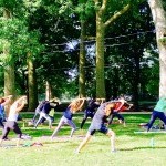 group of women with back to us facing trees, All are lunging to the right with both arms stretched over toward right