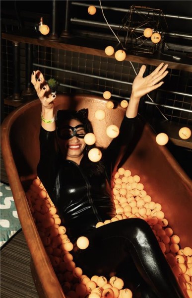 A person in a Cat Costume laying in a bathtub with ping pong balls